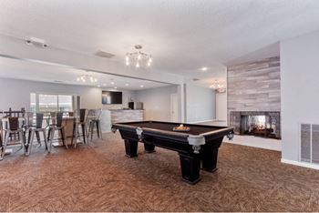 A pool table is in the middle of a room with a fireplace on the wall.